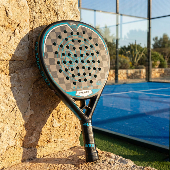Der OLIVER Padel Schläger Air Max 930, schwarz mit blauem Design, lehnt an einer Steinwand, im Hintergrund befindet sich ein Padel-Court