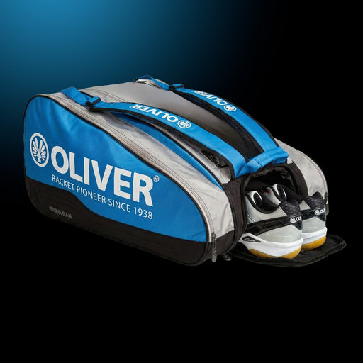 OLIVER Gearbag Extend in blau, grau und schwarzer Farbe mit geöffnetem Schuhfach und OLIVER CX Pro 12 Sportschuhen auf dunklem Hintergrund.