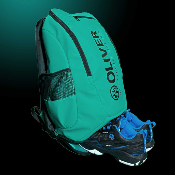 Rucksack Extend von OLIVER in türkisgrün mit geöffnetem Schuhfach und OLIVER Sportschuhen auf dunklem Hintergrund.