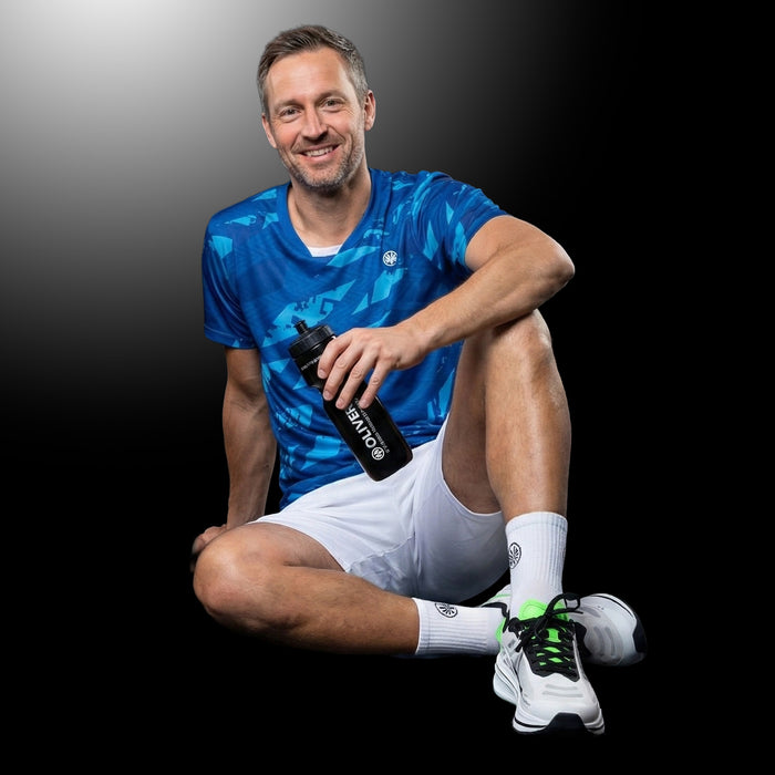 Sportler in OLIVER Sportbekleidung hält schwarze OLIVER Sport Trinkflasche mit weißem Logo und weißer Schrift auf dunklem Hintergrund.